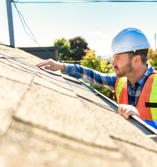 man with hard hat standing on steps inspecting house roof